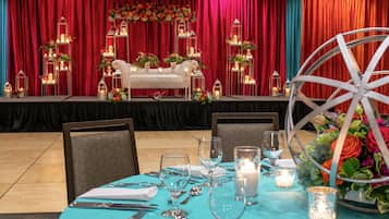 A formal dining setup with a table set for four, a stage with floral decorations, and a large wheel in the foreground.