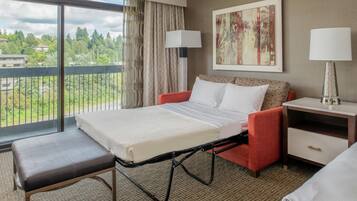 A hotel room with a bed, a bench, a nightstand, and a view of a balcony.