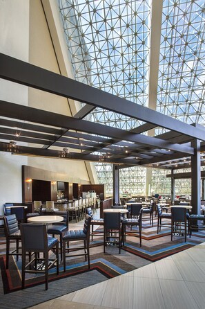 A spacious indoor area with a high ceiling and a geometric glass structure. There are multiple seating areas with tables and chairs.