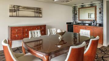 A dining area with a wooden table, white upholstered chairs, a wooden sideboard, and a large mirror above the counter.