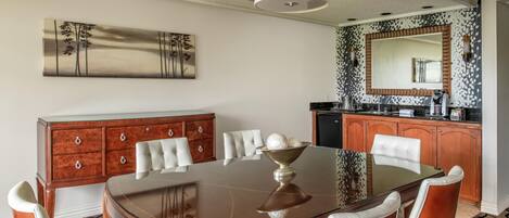 A dining area with a wooden table, white upholstered chairs, a wooden sideboard, and a large mirror above the counter.