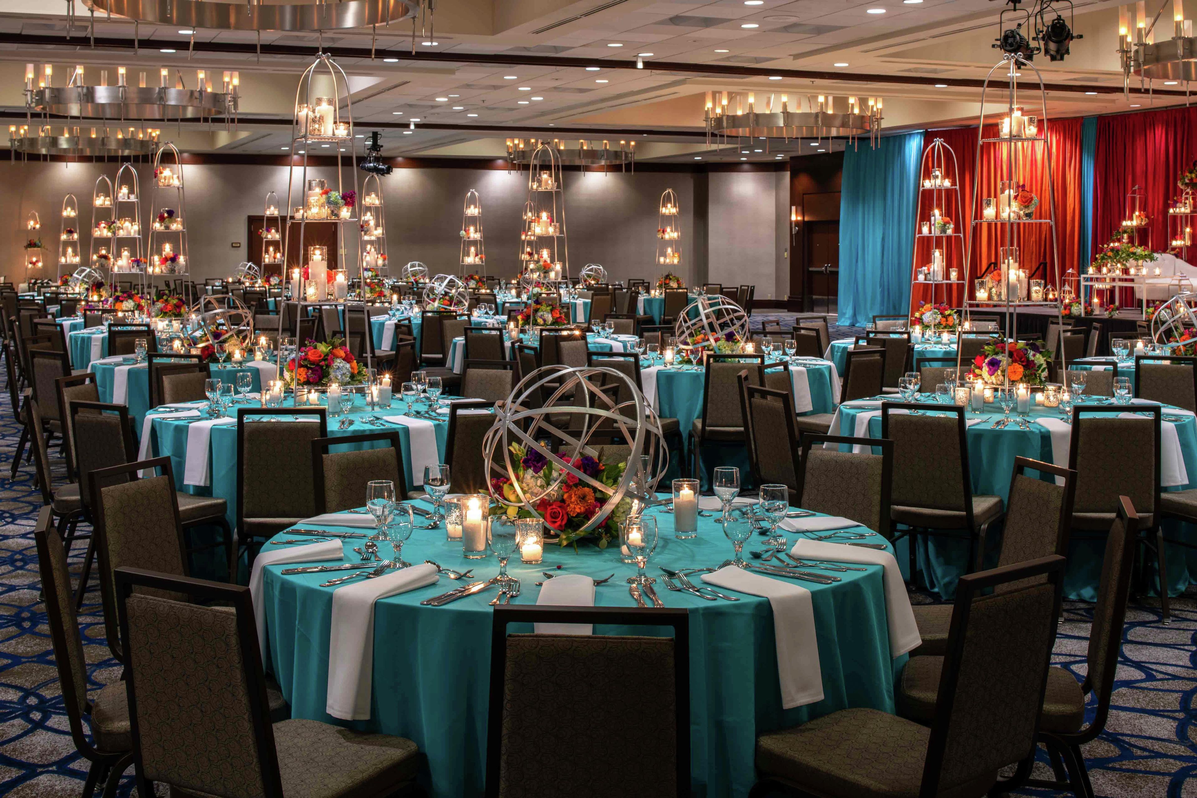 Une salle de banquet avec des tables rondes dressées pour le repas, agrémentées de nappes couleur turquoise et de centres de table floraux.