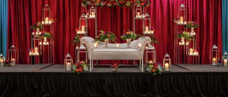 A stage with a white sofa, red curtains, and floral arrangements.