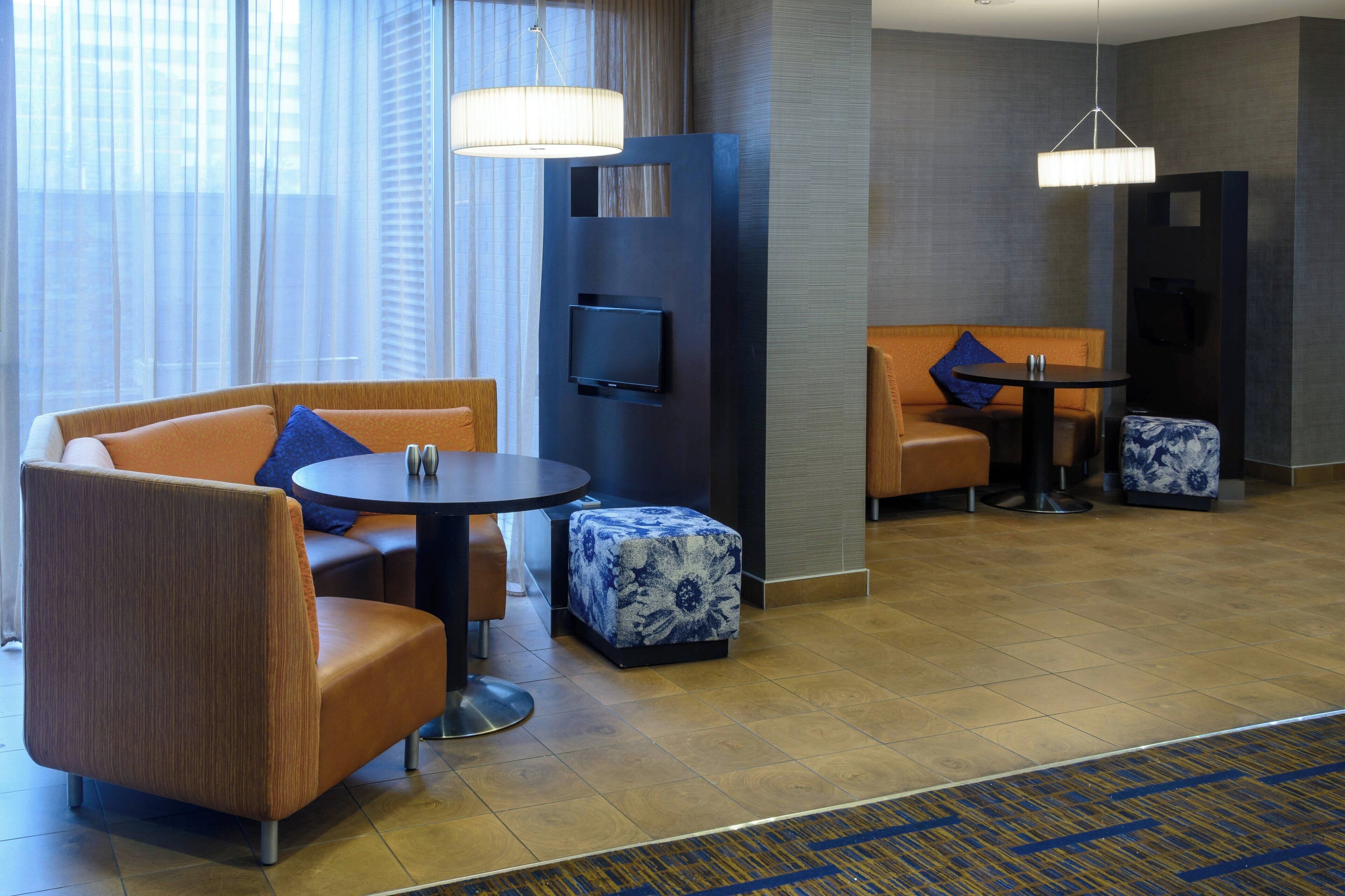 Moderni hotellihuone, jossa on sohva, jalkarahi, pyöreä pöytä sekä pieni oleskelualue, jossa on tuoli ja pöytä.