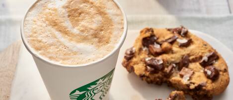 A Starbucks cup with a frothy top and a cookie with chocolate chips on a white plate.