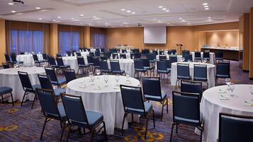 A conference room with multiple round tables, each with chairs and white tablecloths.