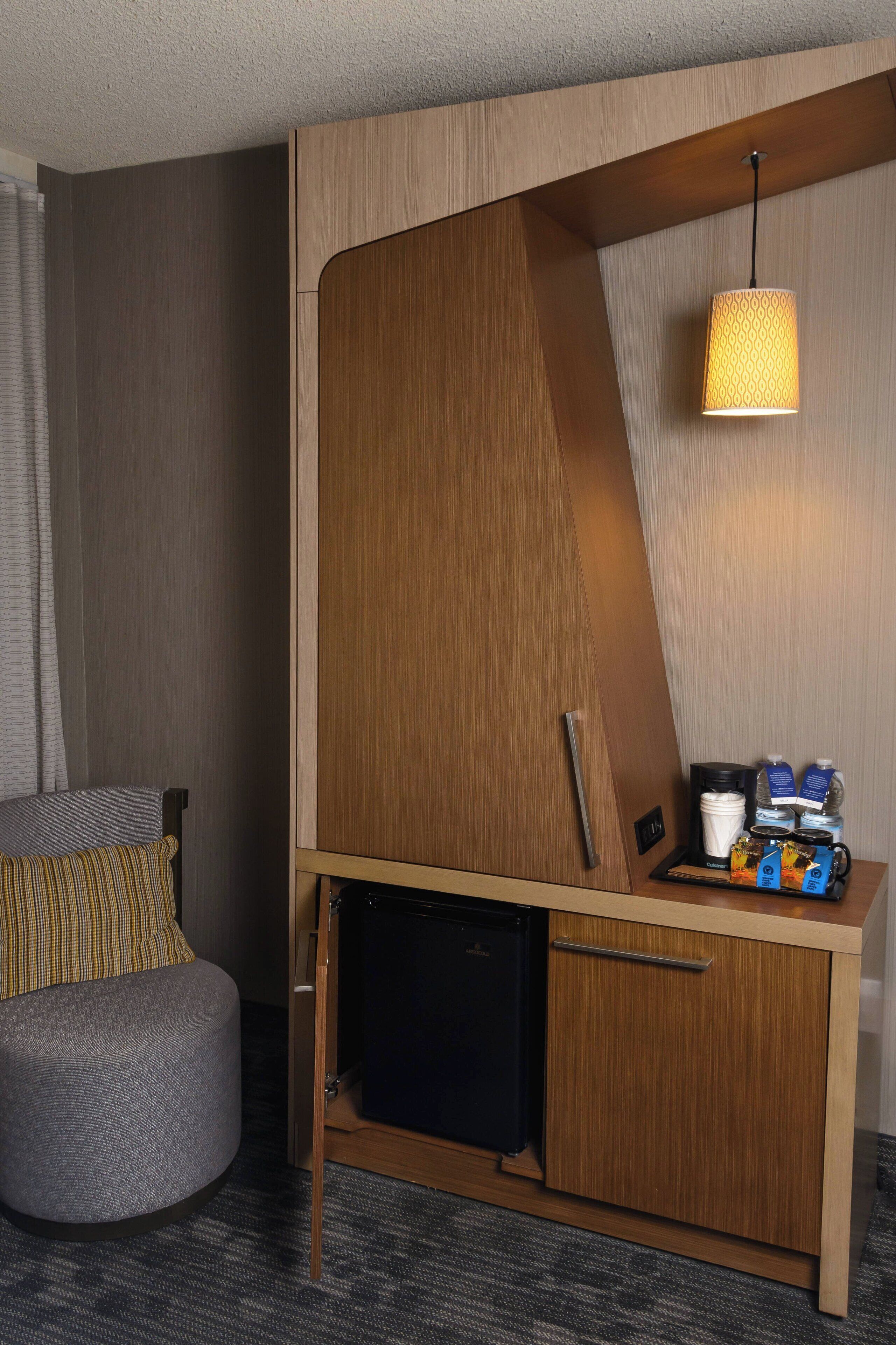 A compact hotel room with a kitchenette, a small seating area, and a hanging lamp.