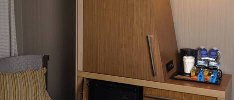A compact hotel room with a kitchenette, a small seating area, and a hanging lamp.