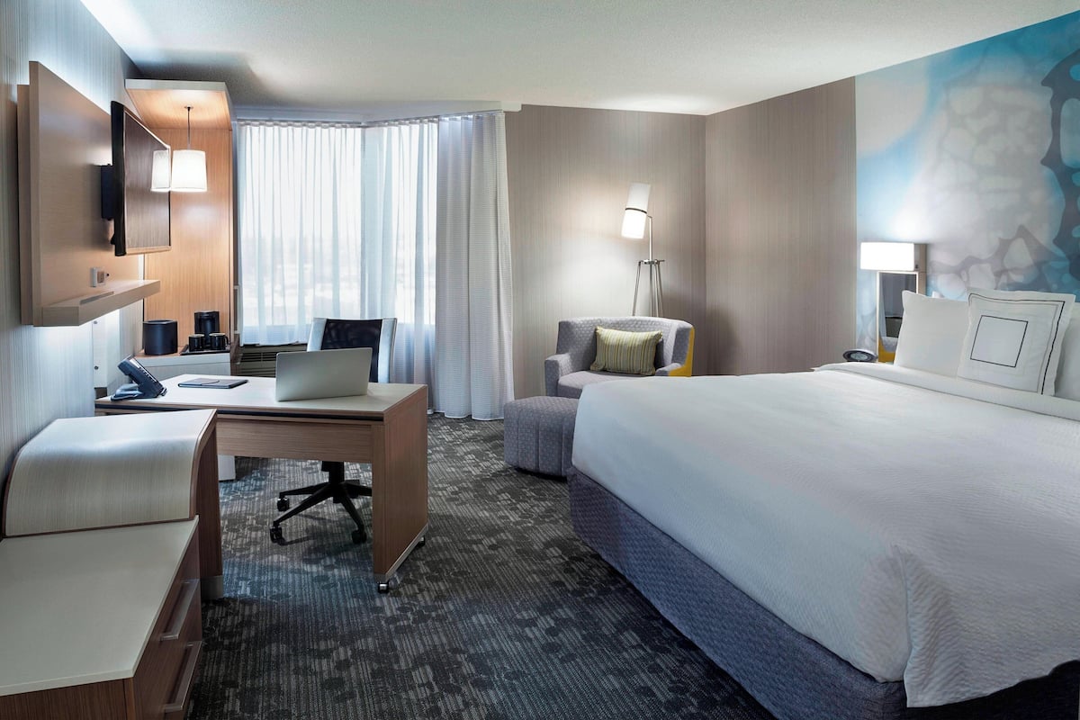 A hotel room with a bed, desk, chair, and a TV.