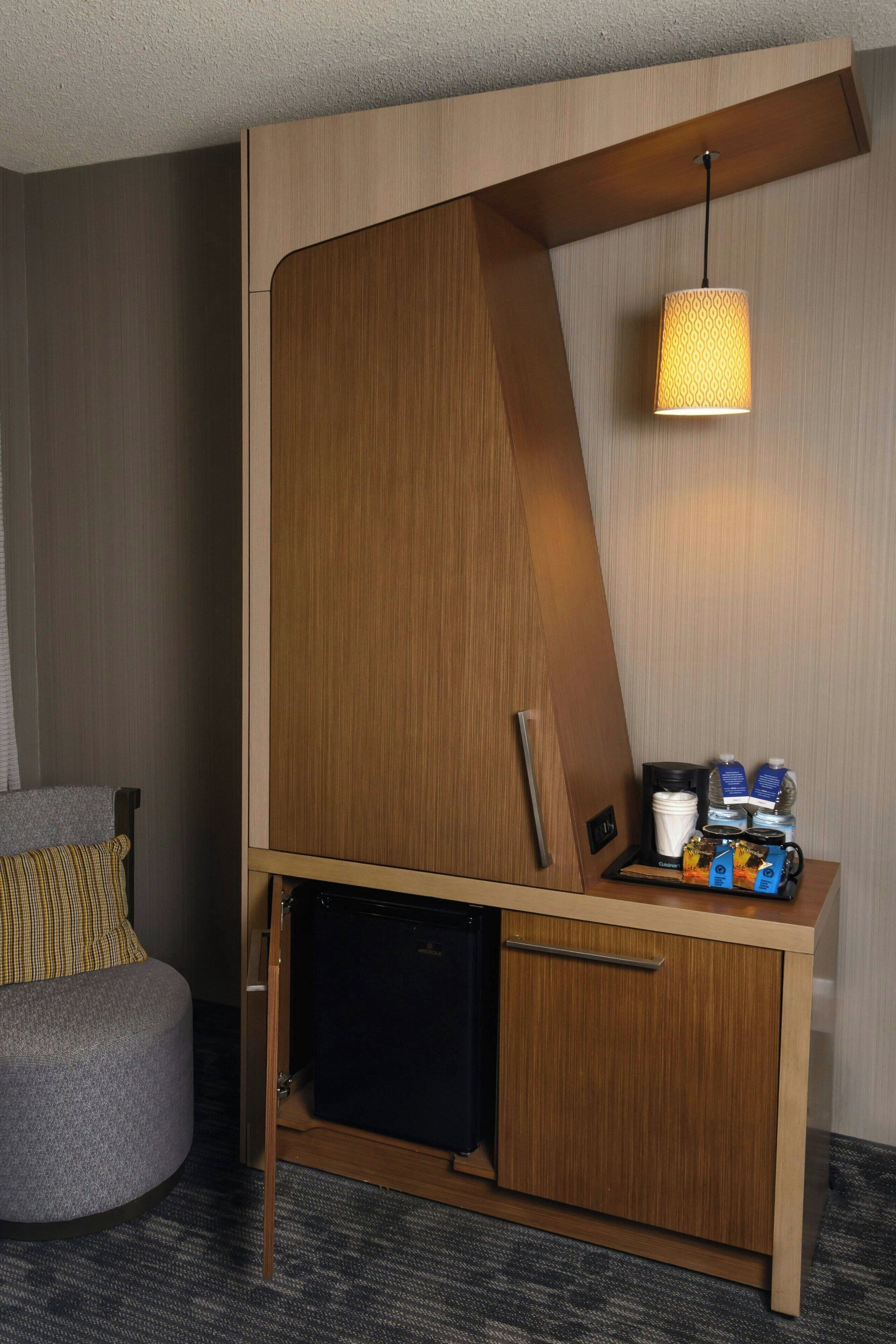 Una habitación de hotel compacta con un escritorio de madera incorporado, un pequeño rincón de descanso y una lámpara colgante.