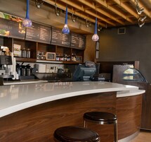 Zona de bar con mostrador de madera, taburetes e iluminación colgante.