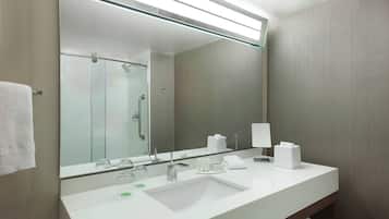 A modern bathroom with a large mirror, white sink, and glass shower enclosure.