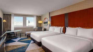 Quarto de hotel com duas camas, uma escrivaninha, uma cadeira, televisão e janela com vista.