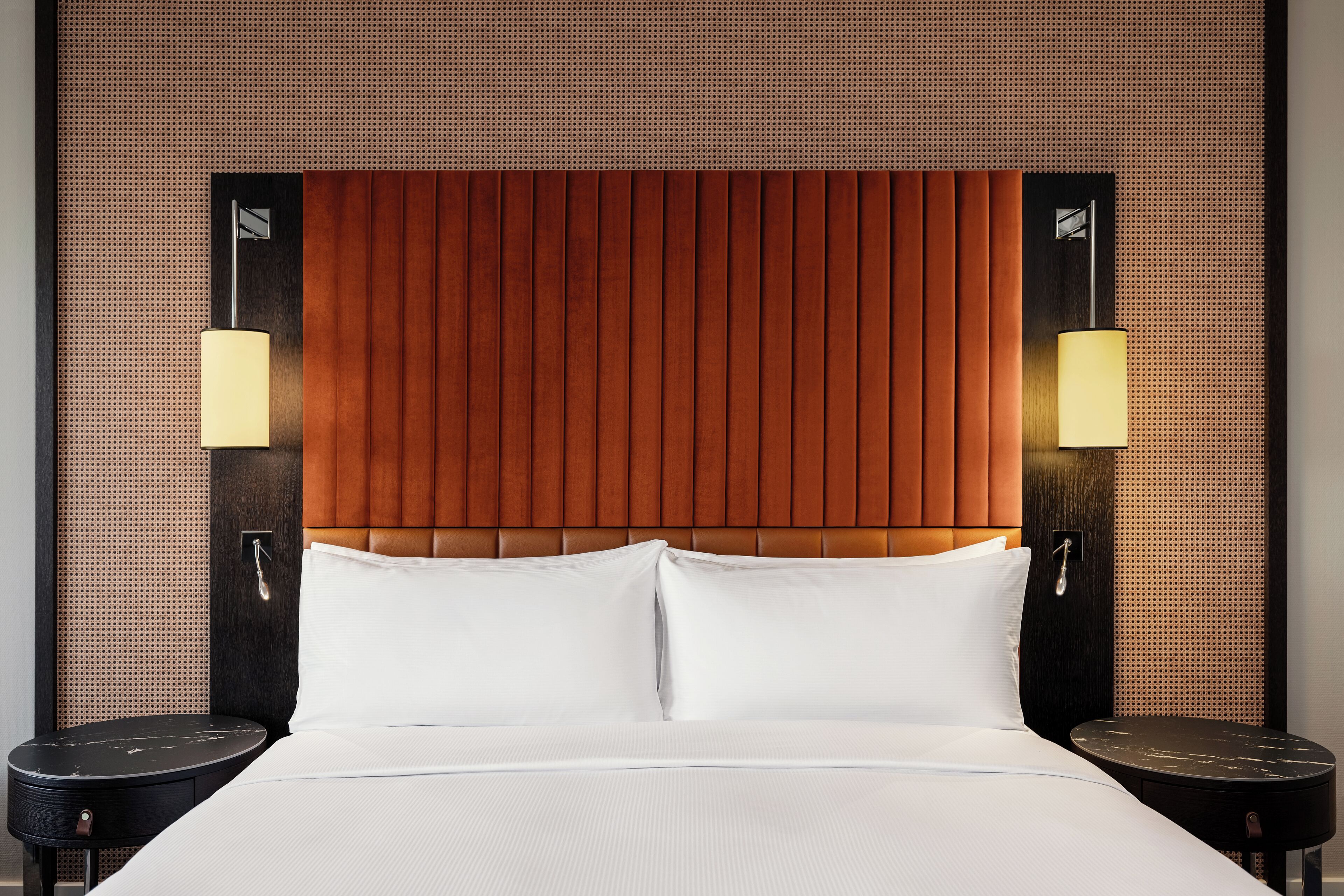 Quarto de hotel com uma cama grande, duas mesas de cabeceira e um painel de cabeceira em madeira.