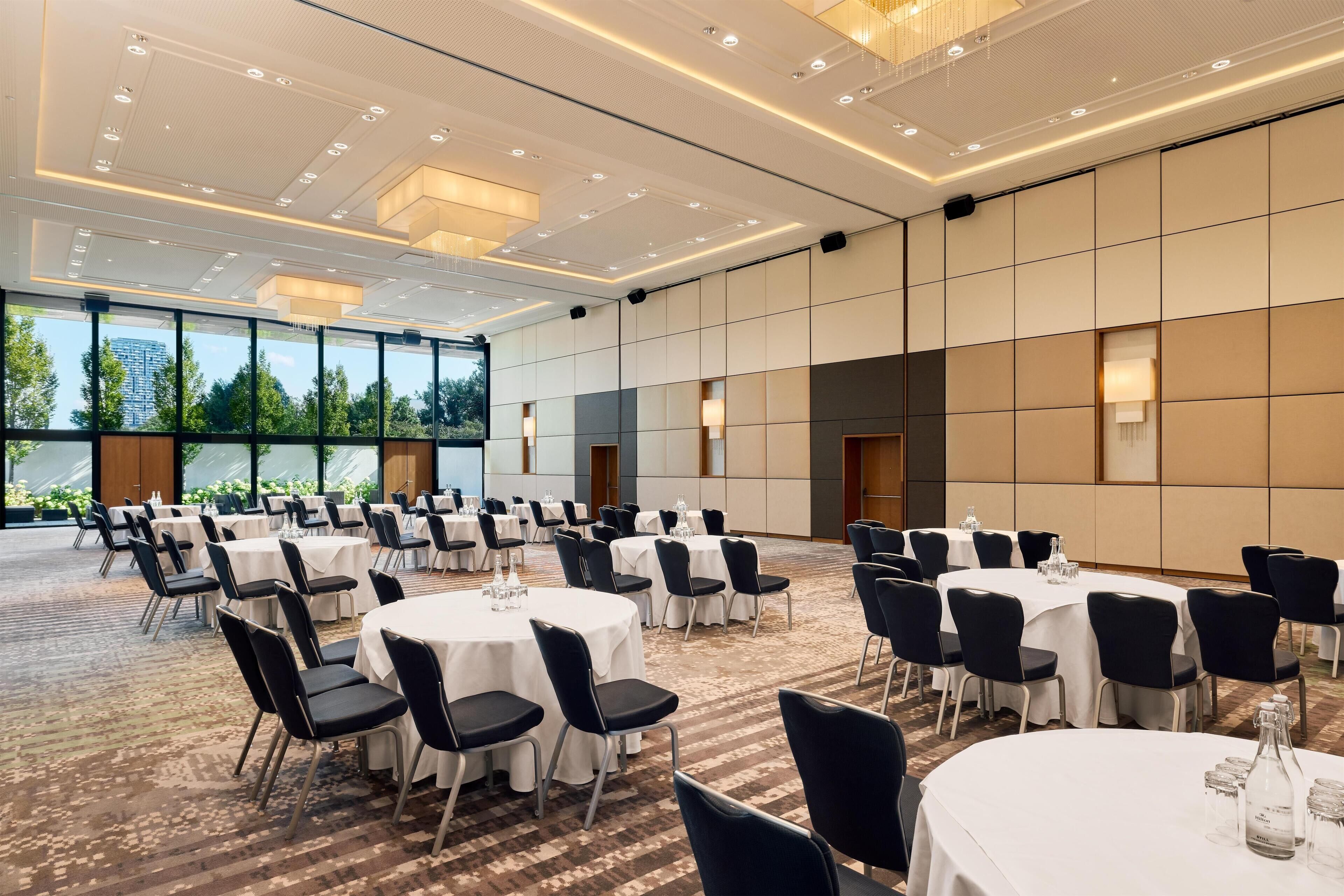 A spacious conference room with multiple round tables, black chairs, and a carpeted floor.