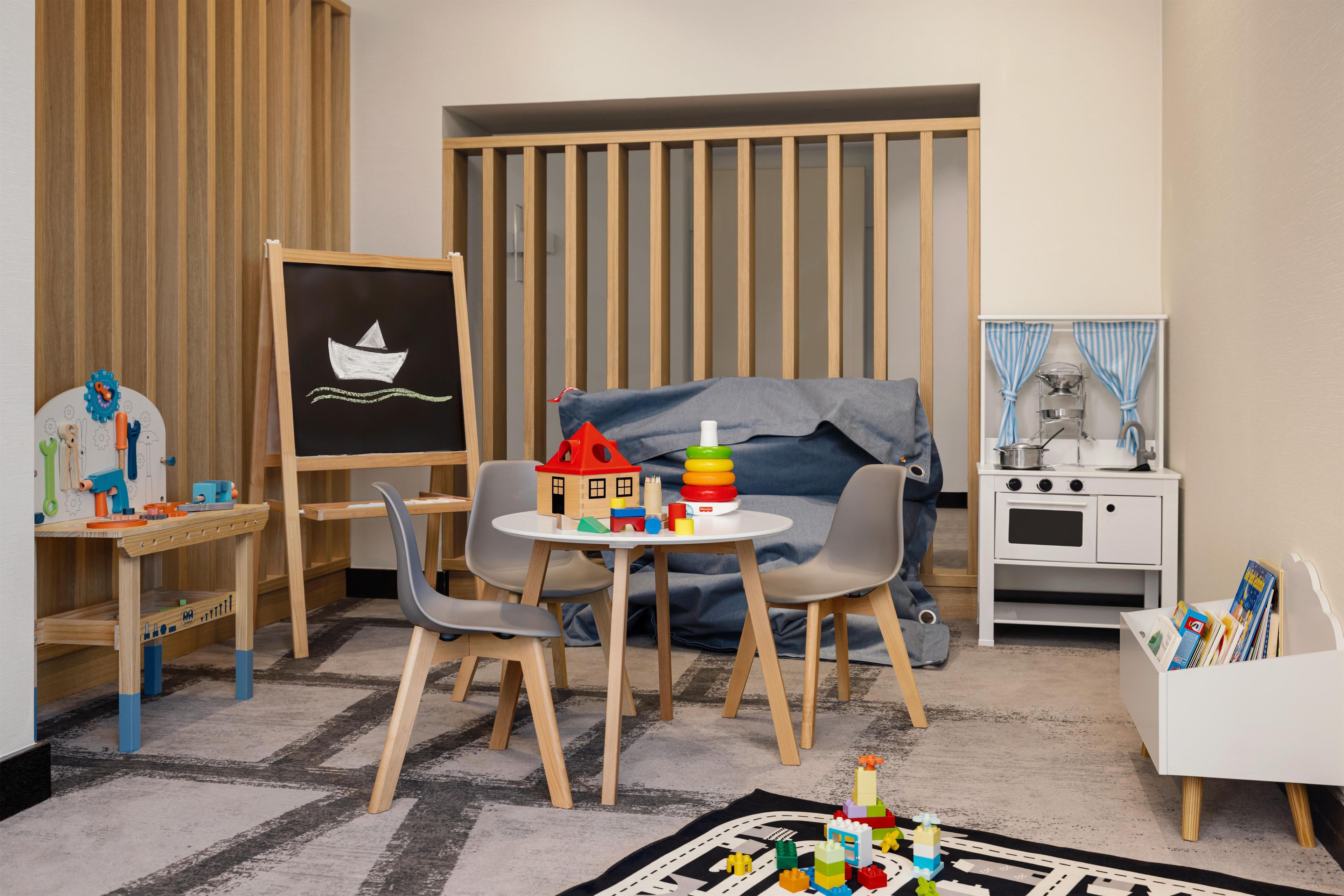 Ein Kinderzimmer mit einem Holztisch, einem kleinen Tischchen, einem Stuhl und einem Bücherregal.