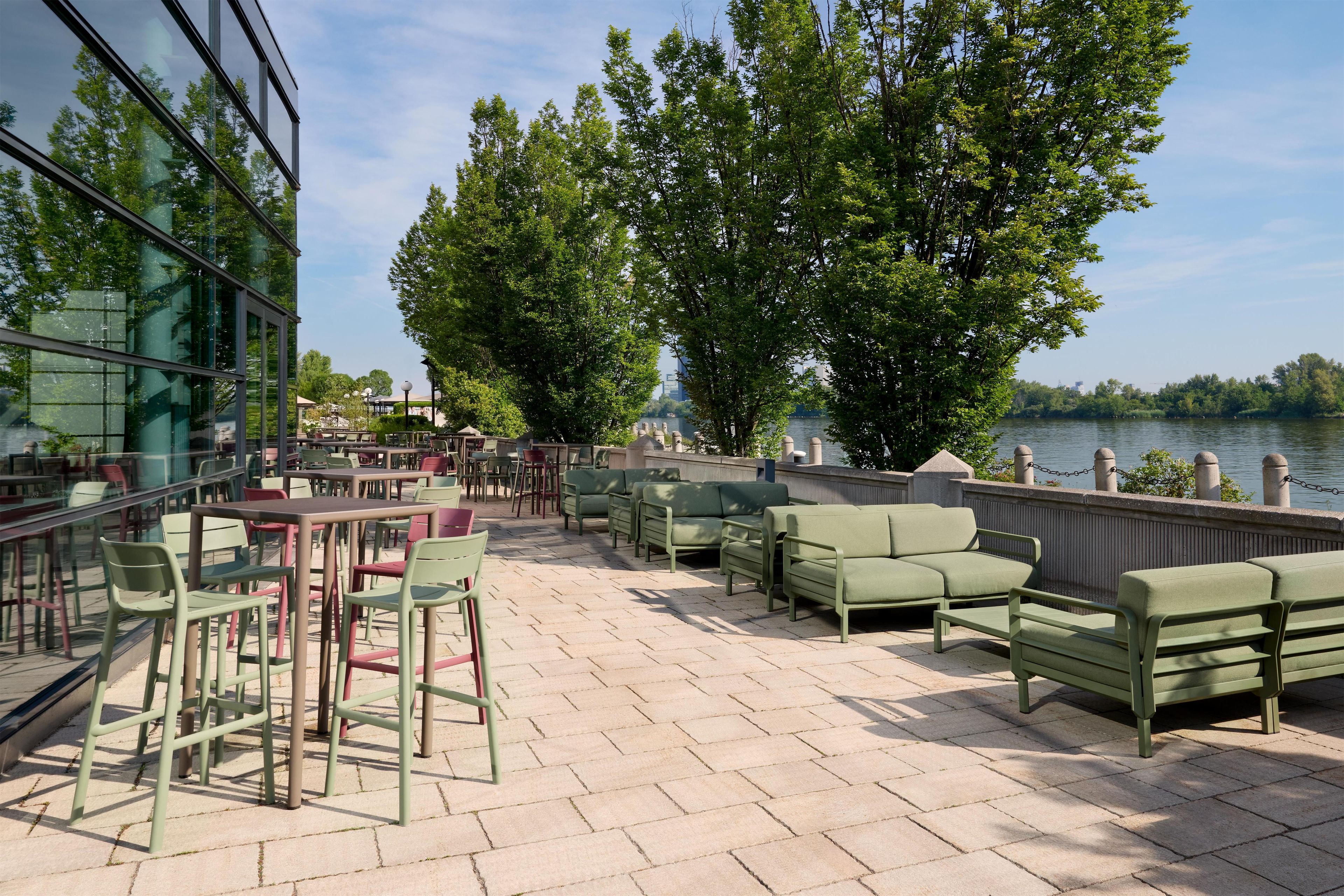 An outdoor seating area with tables and chairs, overlooking a body of water and surrounded by trees.