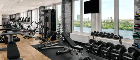 Un gimnasio con máquinas de cardio, equipo de levantamiento de pesas y mancuernas.