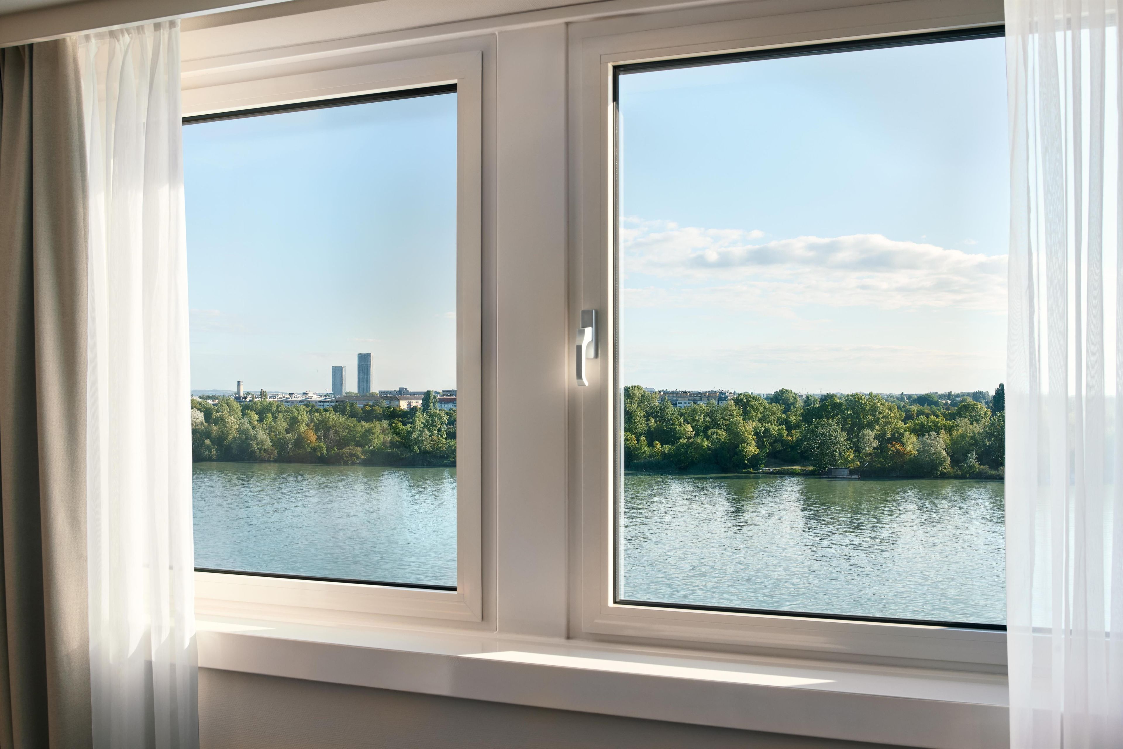Een kamer met een groot raam met uitzicht op een waterpartij en een stadsgezicht.