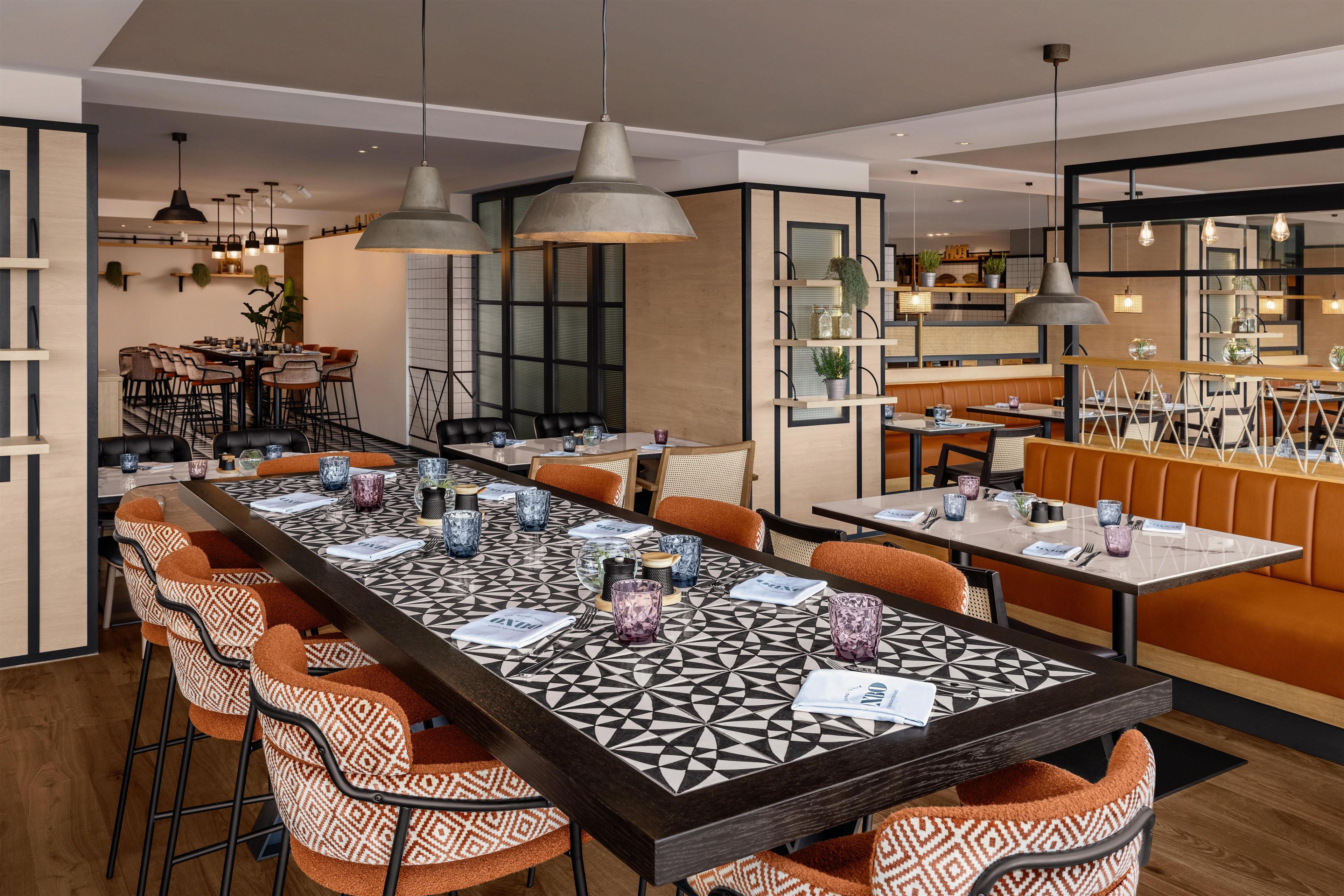 Un restaurante moderno con una mesa común alargada, cabinas individuales e iluminación colgante.