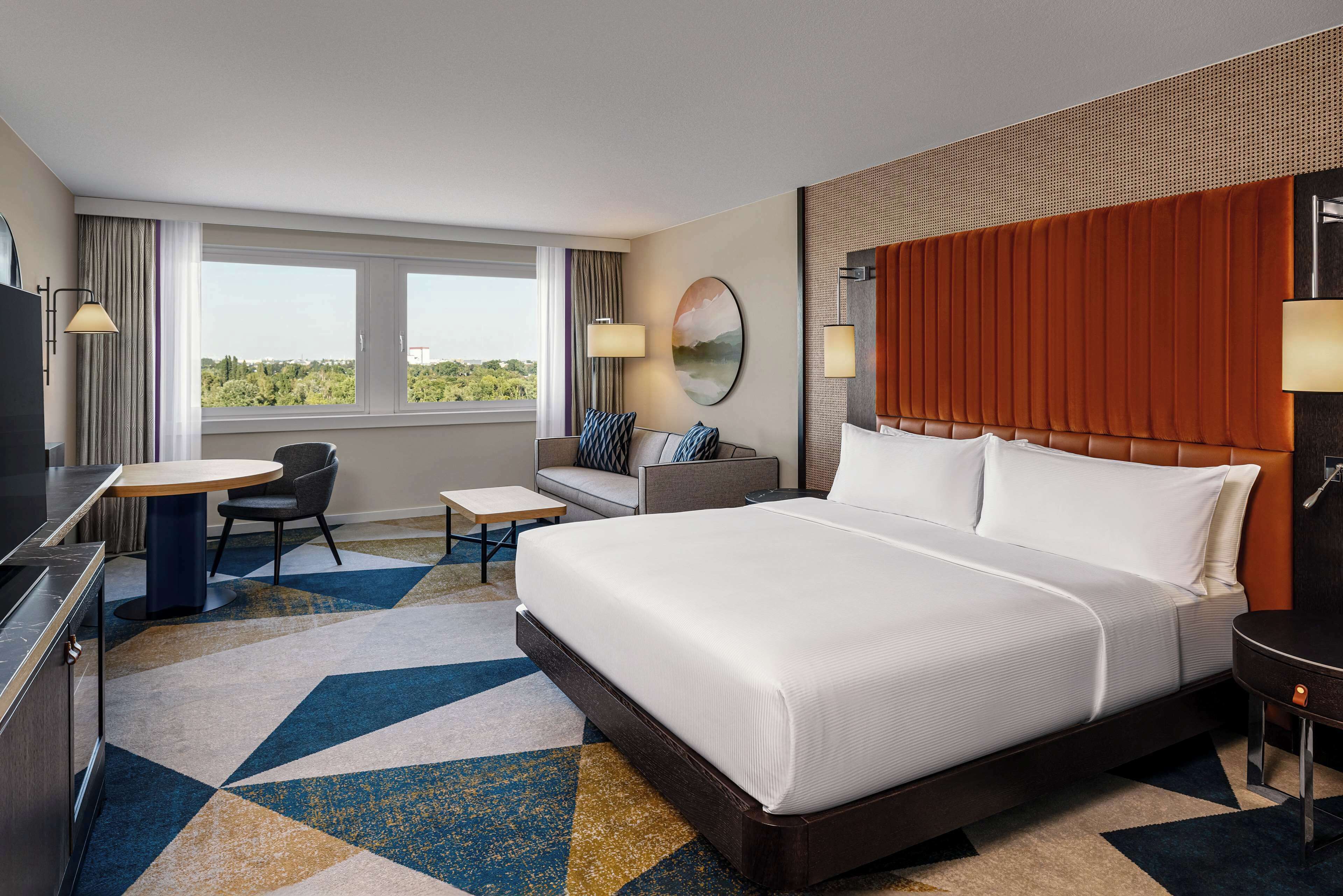 A hotel room with a large bed, a desk, a chair, a TV, and a view of the outdoors.
