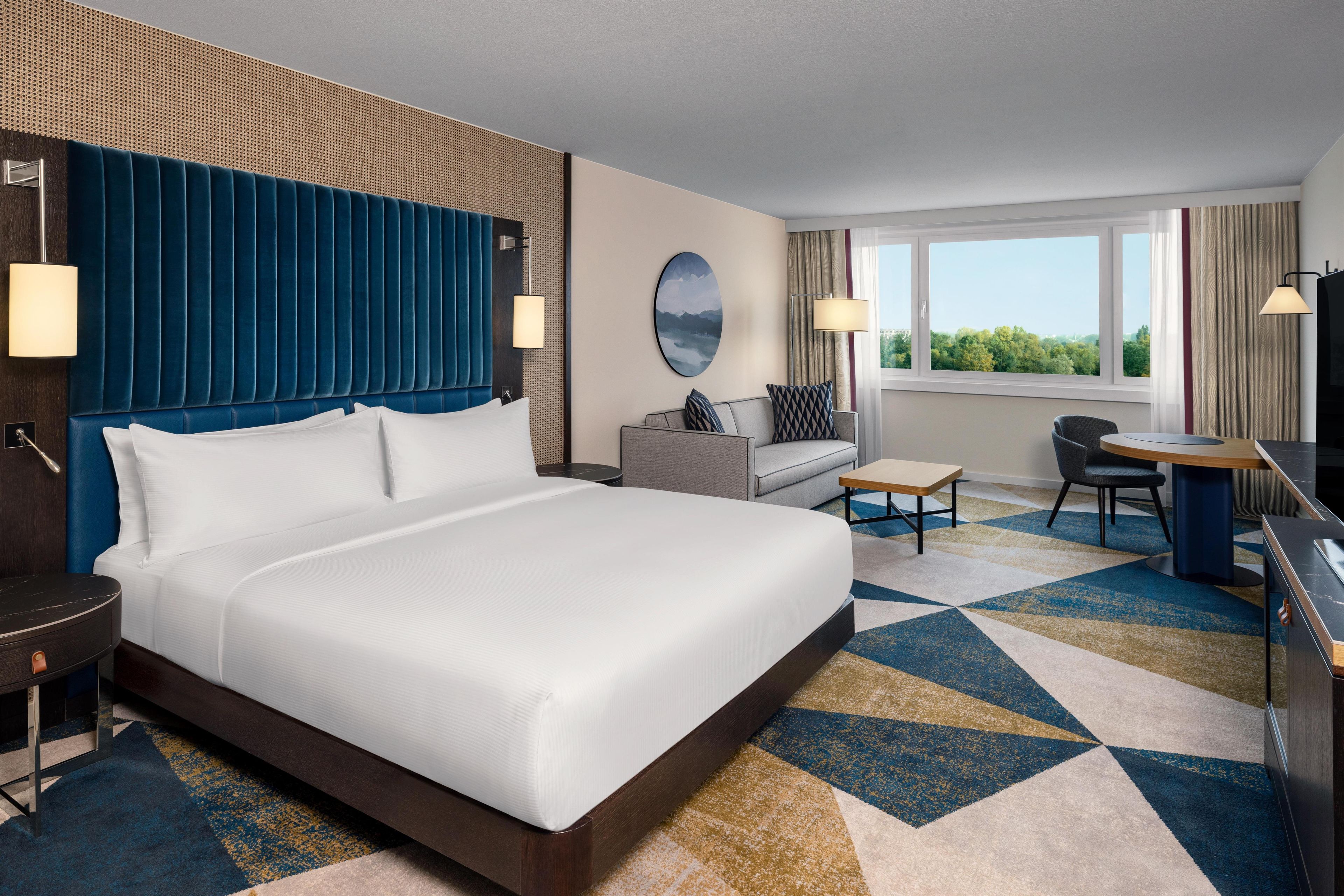 Habitación de hotel con una cama grande, un sofá, un escritorio y vistas al exterior.