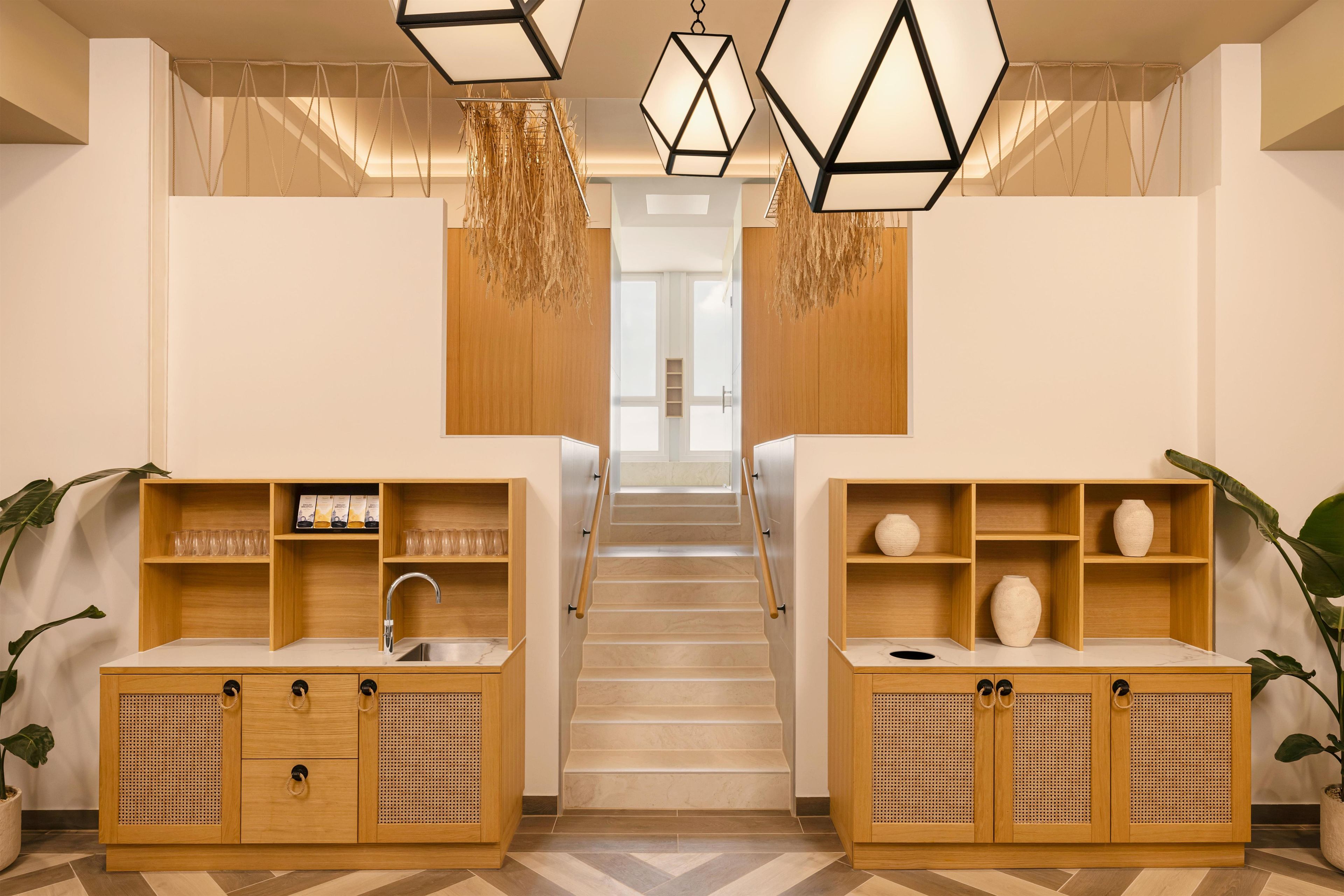 A hotel lobby with a staircase, wooden cabinets, and hanging lights.