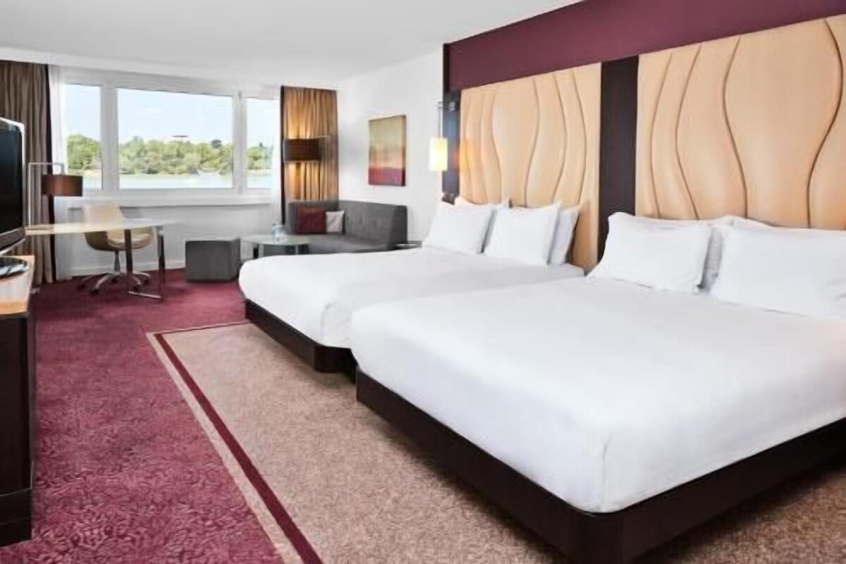 Una habitación de hotel con dos camas, un escritorio, una silla y vistas al exterior.