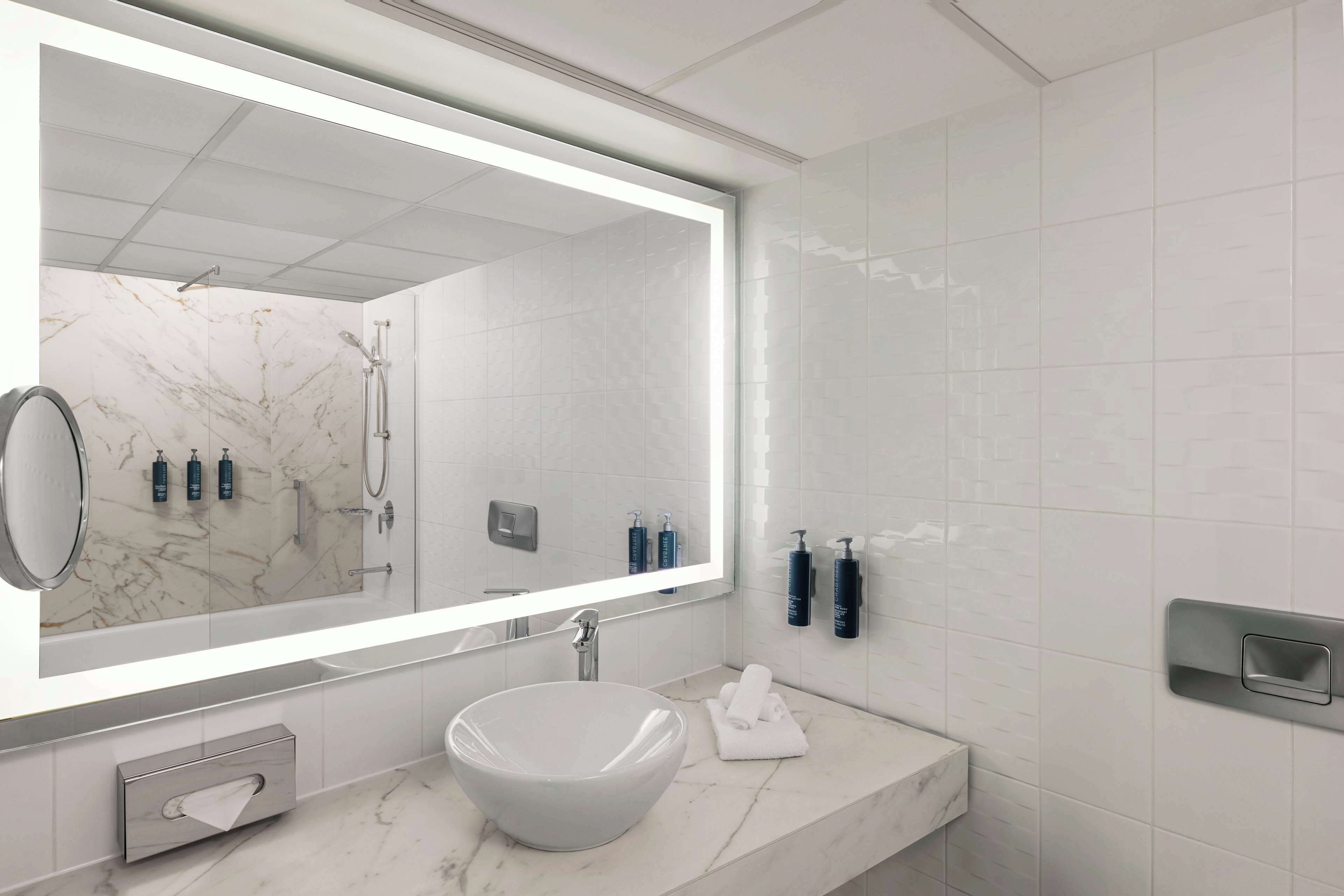 Een moderne badkamer met een grote spiegel, een wastafel van wit marmer en toiletartikelen aan de muur.