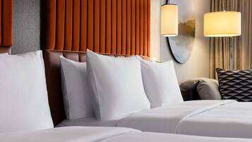 A hotel room with a bed, pillows, a headboard, and a wall-mounted lamp.