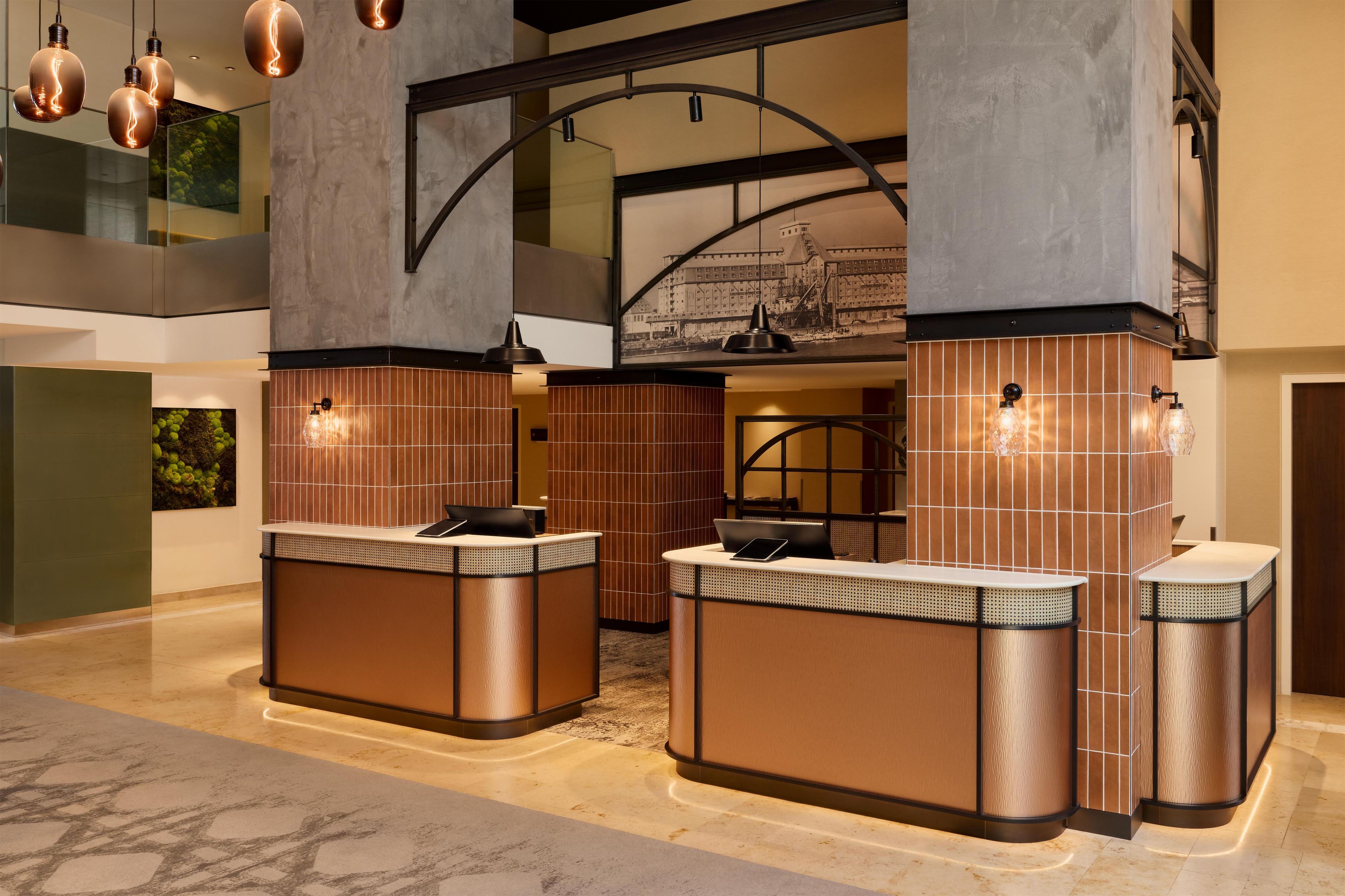 A modern lobby with a reception desk, a large mural, and a high ceiling with hanging lights.