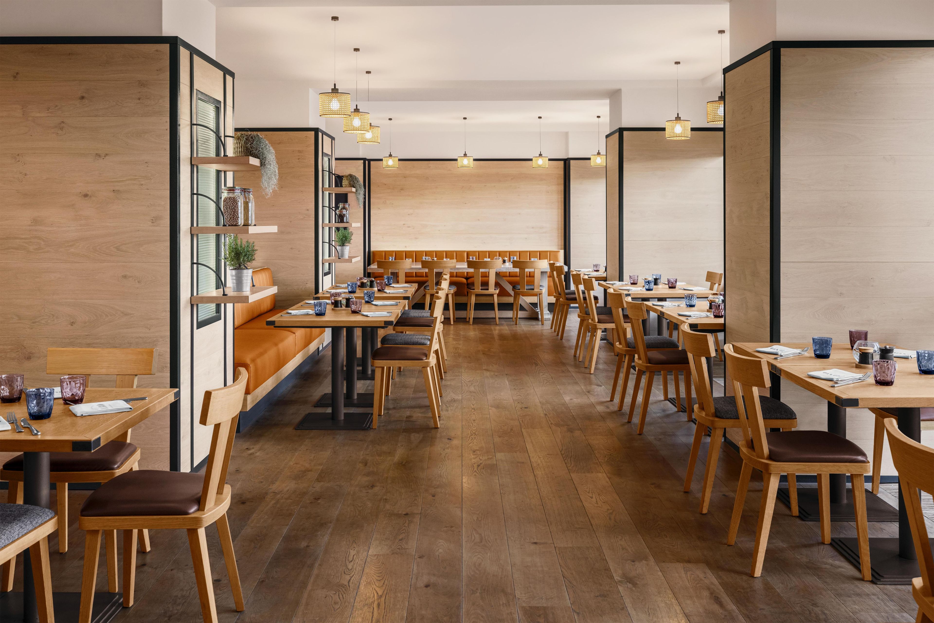 A restaurant with wooden flooring, multiple tables and chairs, and hanging pendant lights.