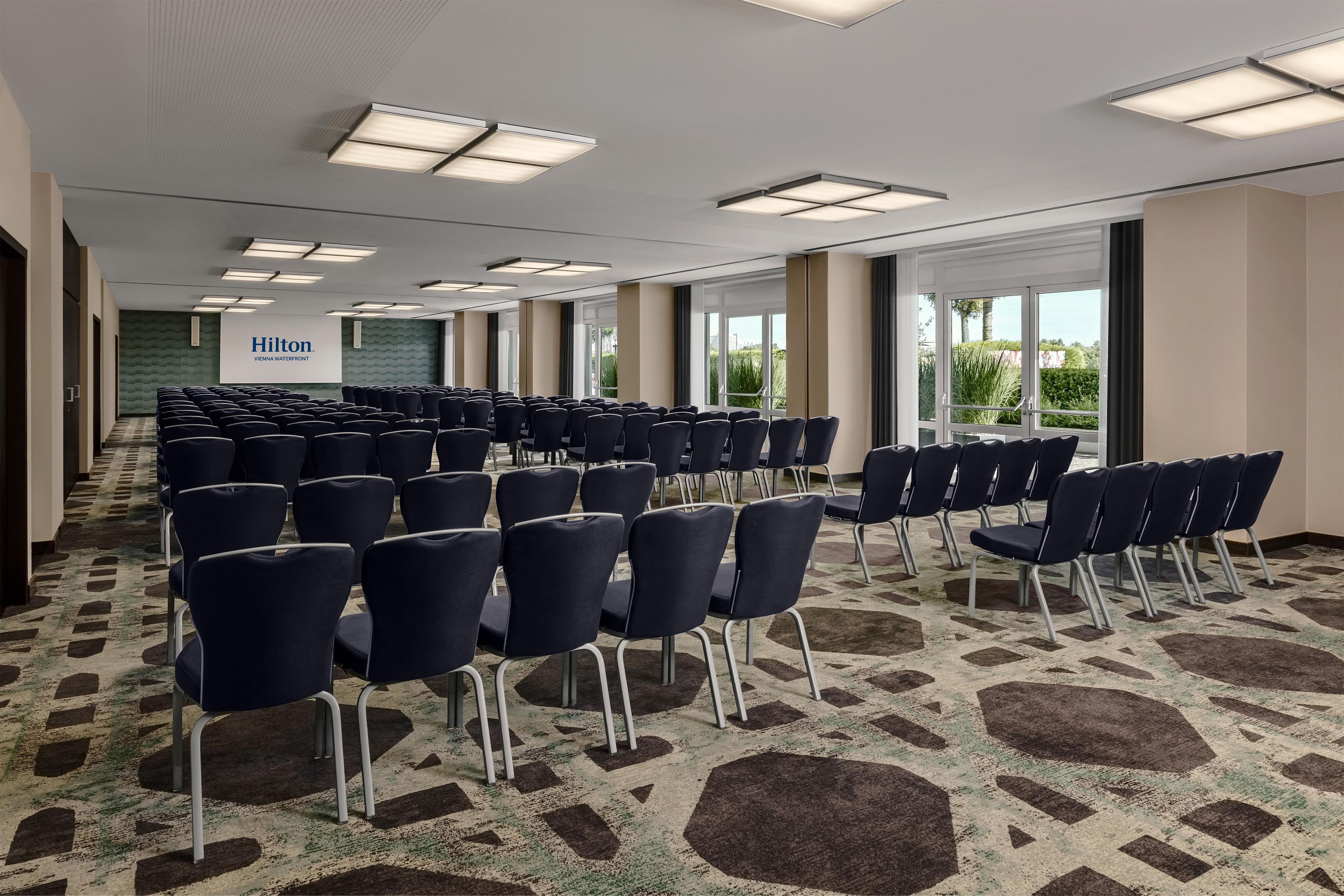 Ein Konferenzraum mit Tischen und Stühlen, großen Fenstern und einem Hilton-Schild.