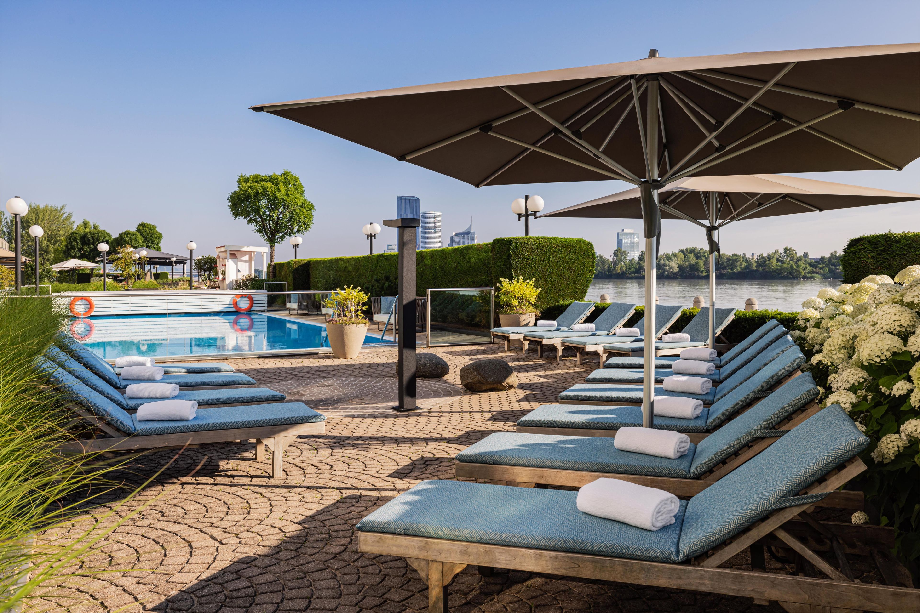 Ein Poolbereich mit Liegestühlen, Sonnenschirmen und Blick auf ein Gewässer.