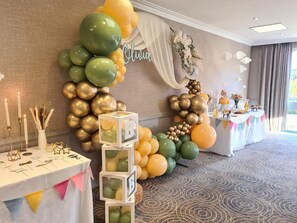 A decorated event space with a balloon arch, a table with food, and a name sign. - Hilton Cobham (Cobham)