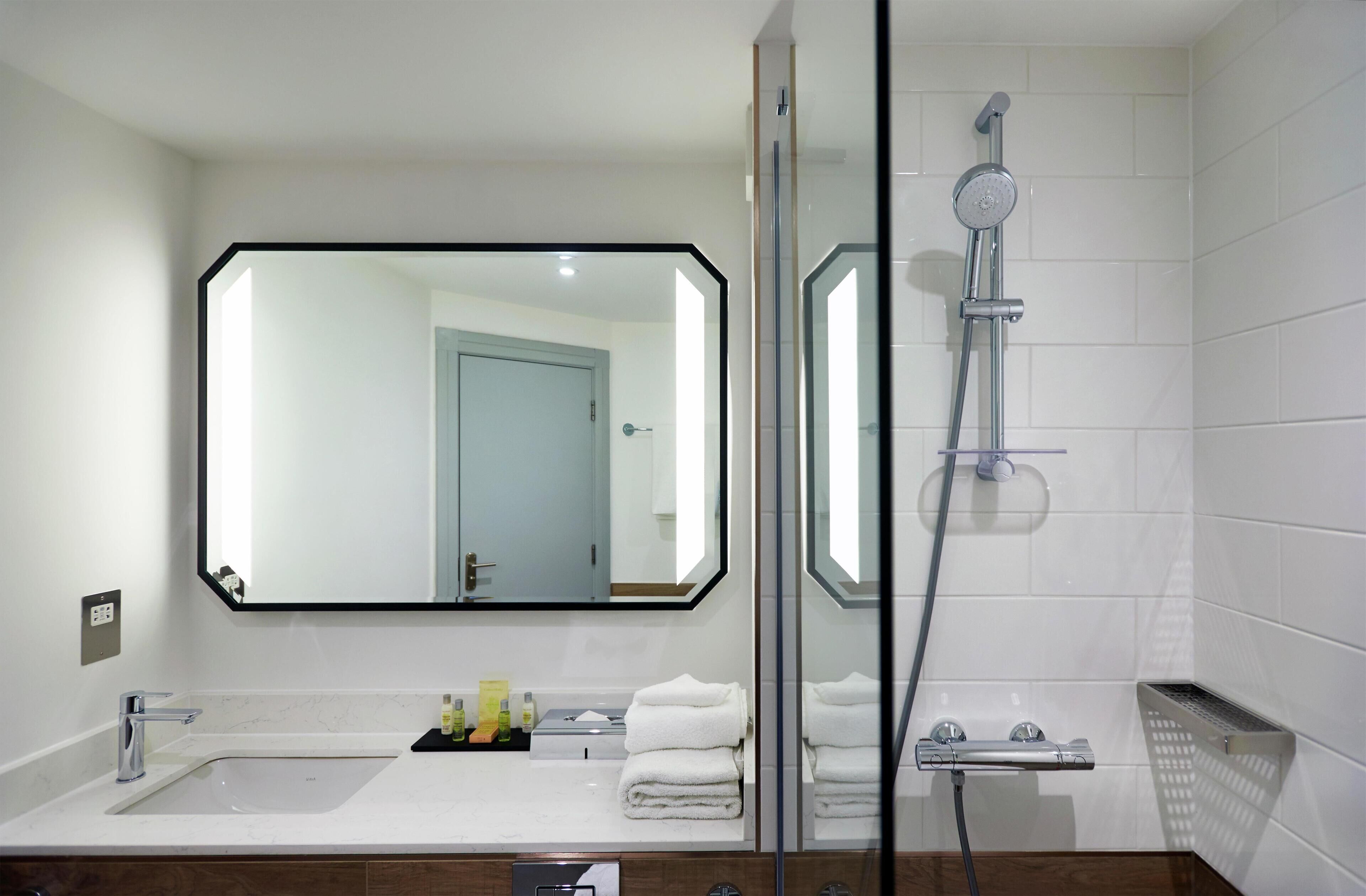 A modern bathroom with a large mirror, a shower, a sink, and neatly folded towels.