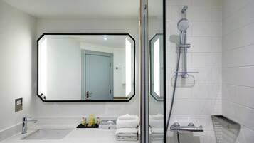 A modern bathroom with a large mirror, a shower, a sink, and neatly folded towels.