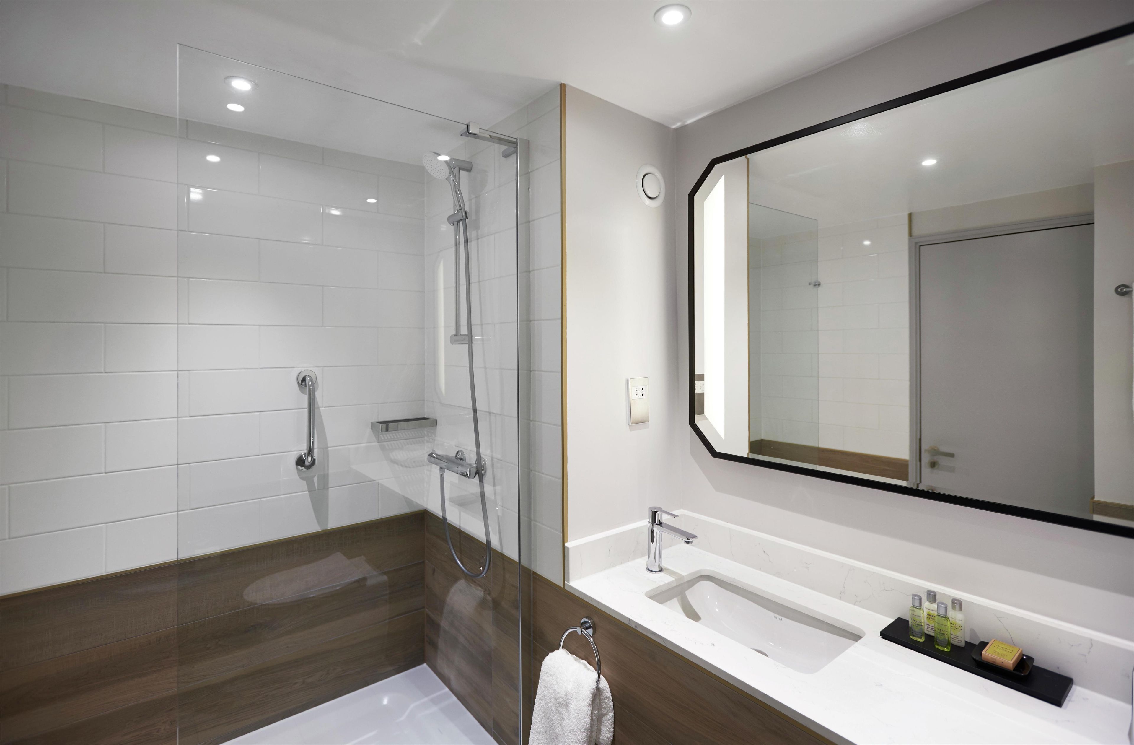 A modern bathroom with a glass-enclosed shower, a large mirror, and a white sink with toiletries.