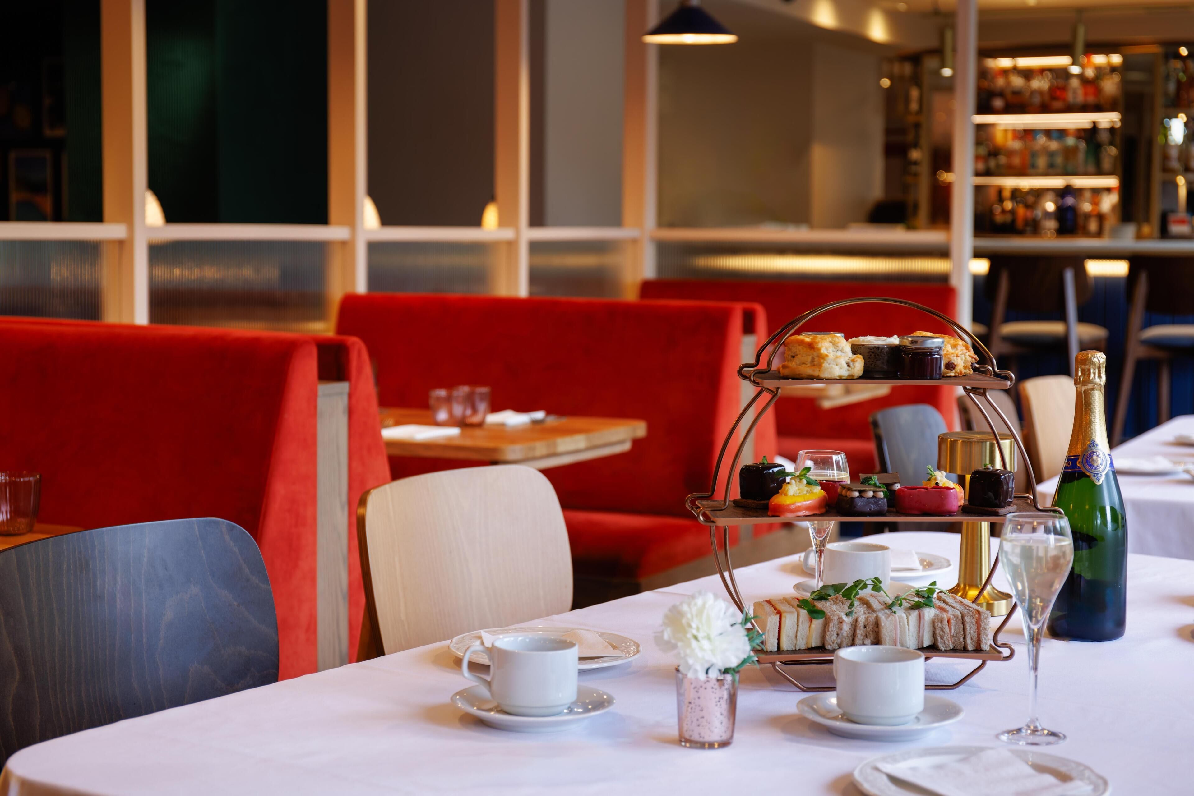 A dining table with a tiered dessert stand, white tableware, and a bottle of champagne.