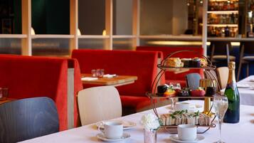 A dining table with a tiered dessert stand, white tableware, and a bottle of champagne.