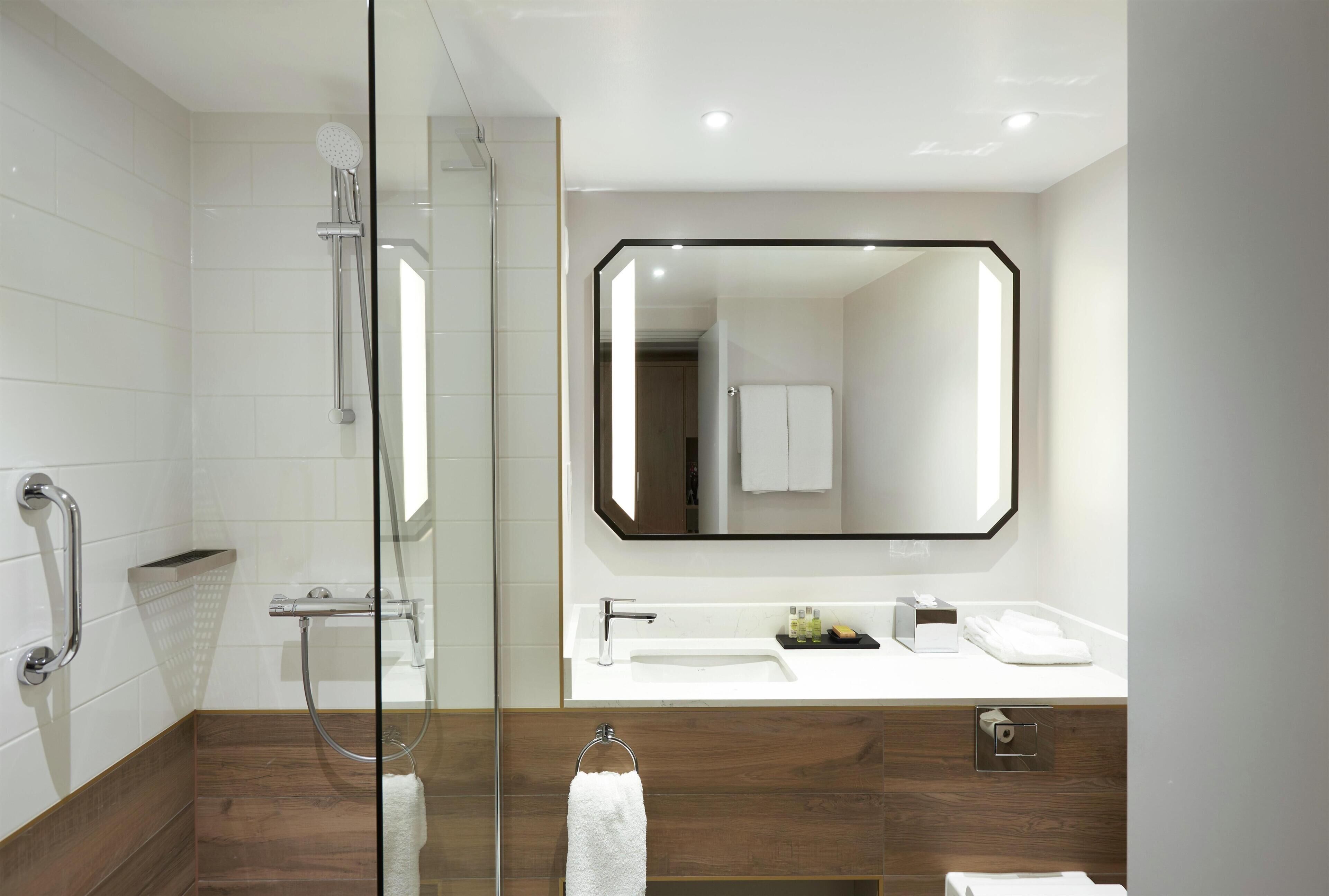 Un baño moderno con cabina de ducha de vidrio, un espejo grande y un mueble de tocador de madera.