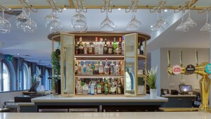A bar area with shelves of liquor bottles, a cash register, and a beer tap. - Hilton Cobham (Cobham)