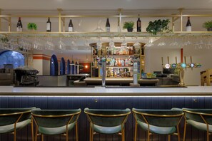 A bar area with a counter, bar stools, and a variety of bottles and glasses. - Hilton Cobham (Cobham)