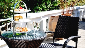 A round glass table with a wicker chair, a tiered dessert stand, and glasses of champagne. - Hilton Cobham (Cobham)