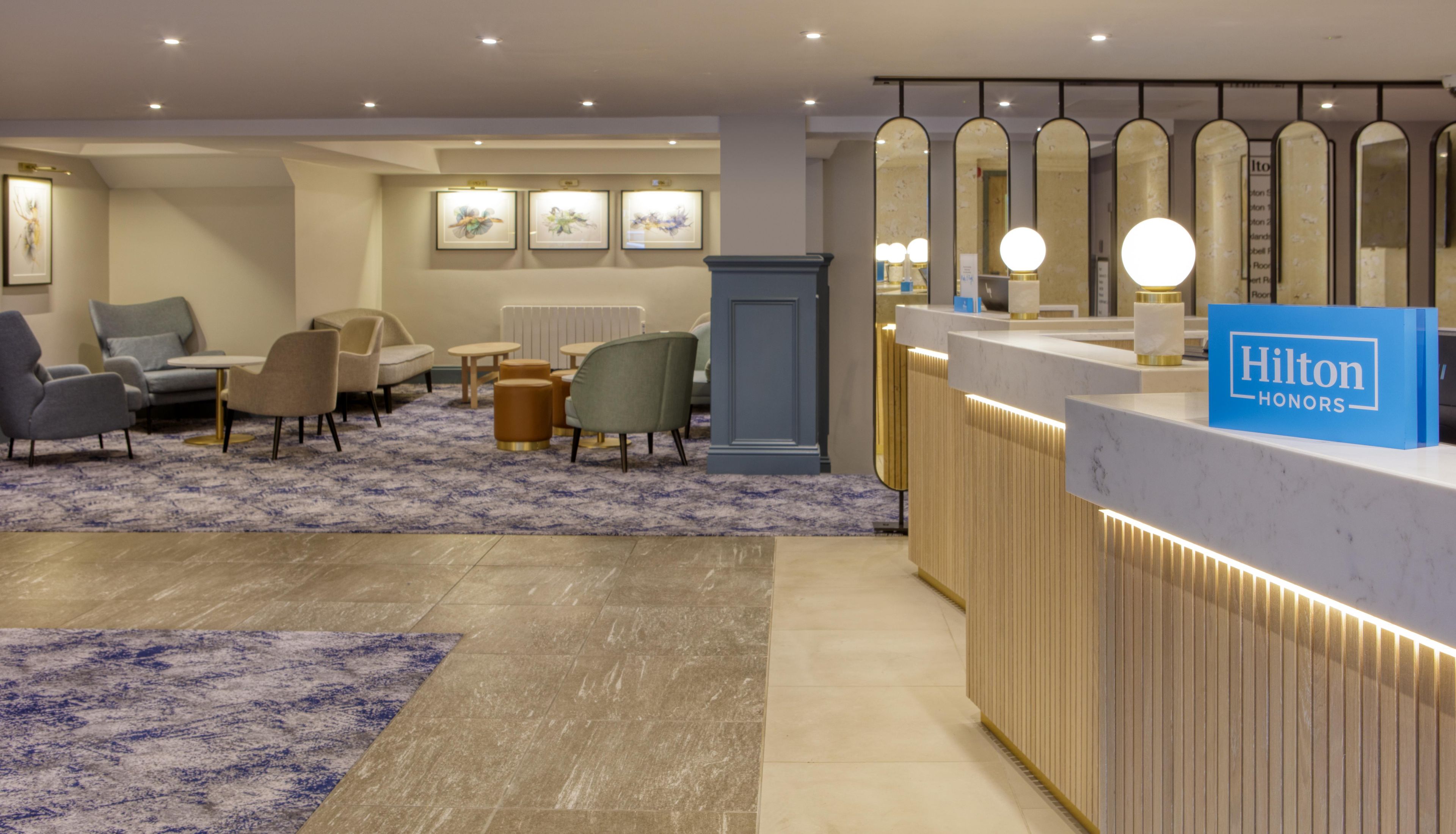 A hotel reception area with a blue sign, seating, artwork on the wall, and a patterned carpet.
