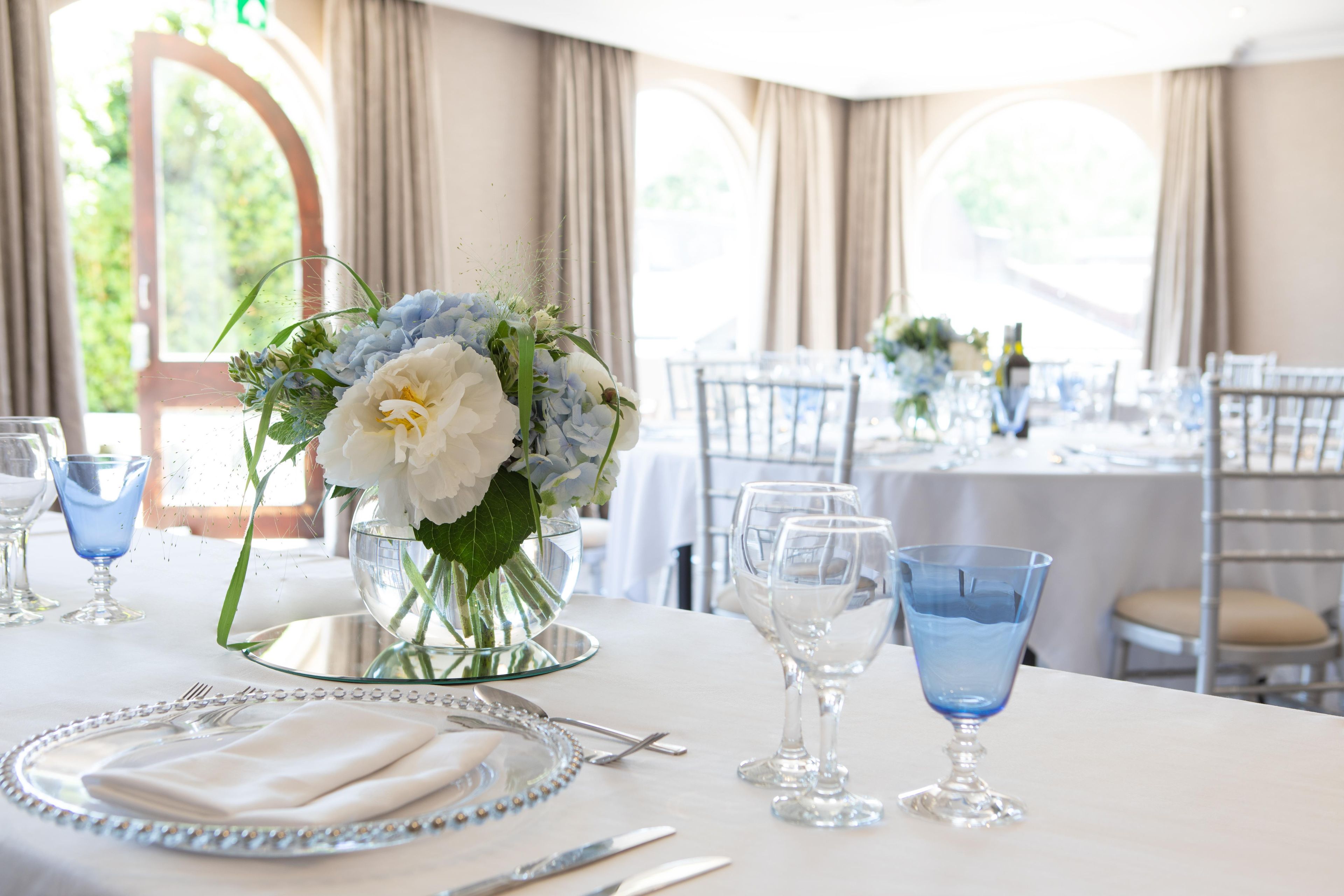 A dining table set with a vase of flowers, glasses, and cutlery.