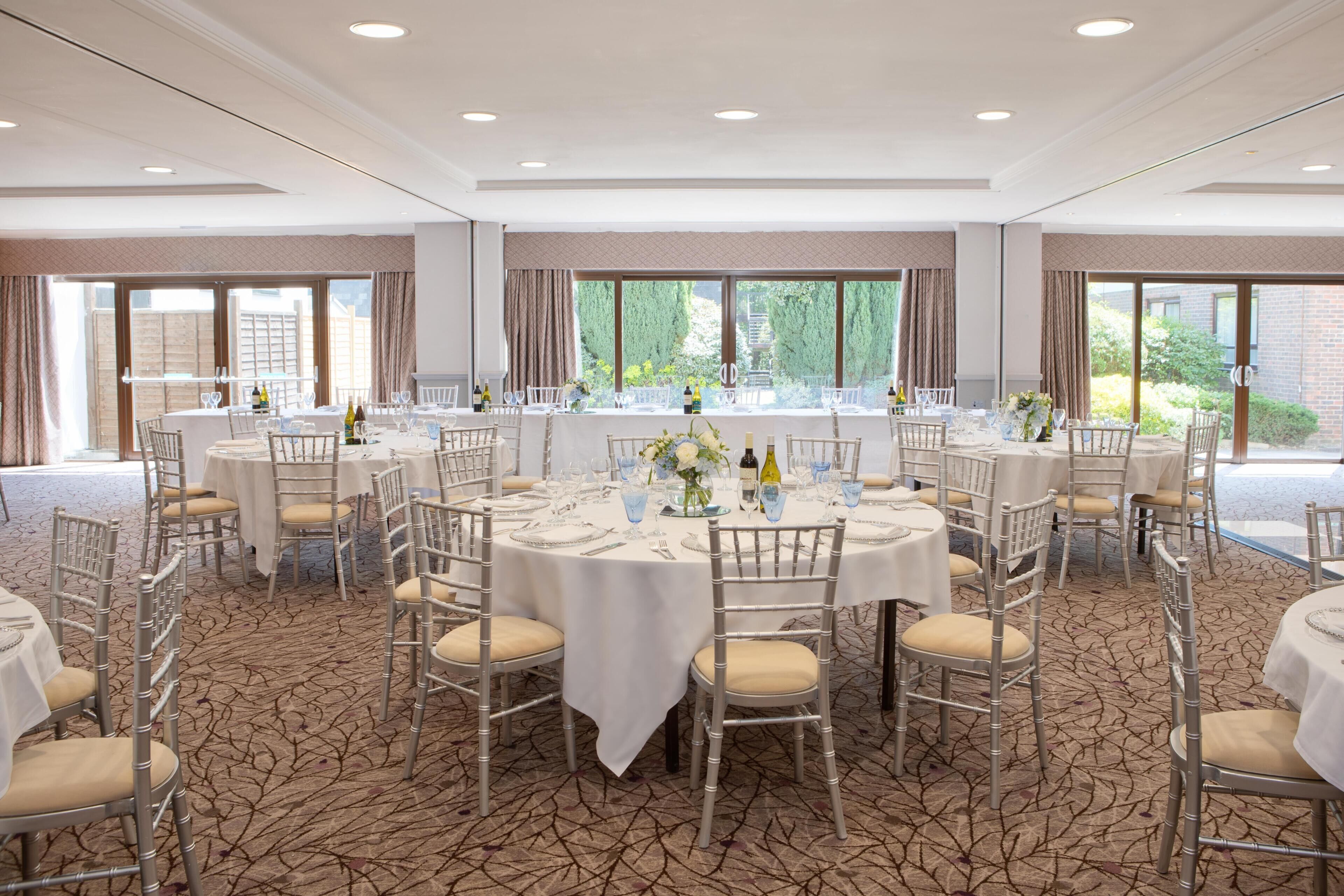 Juhlava tila, jossa on pyöreitä pöytiä, tuoleja ja matolla peitetty lattia.