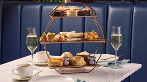 A three-tiered dessert stand with various pastries and jams on a table, accompanied by two glasses of champagne and a cup of tea. - Hilton Cobham (Cobham)