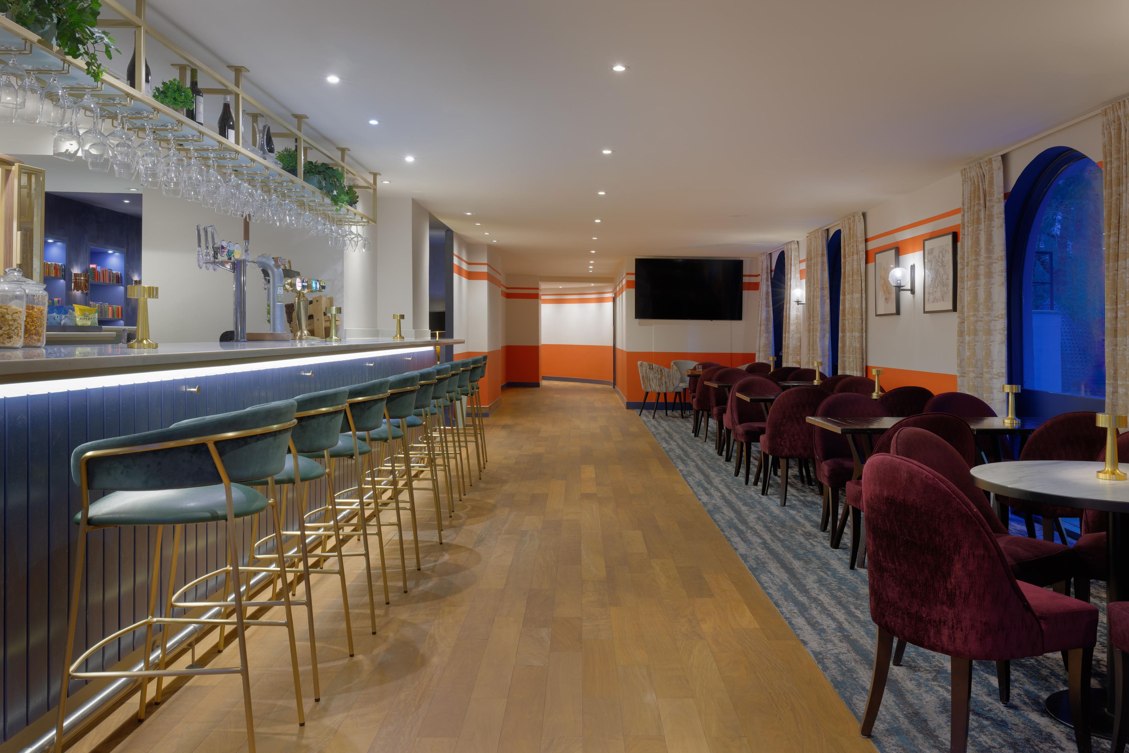 A bar area with stools and a counter, a seating area with tables and chairs, and a television mounted on the wall.