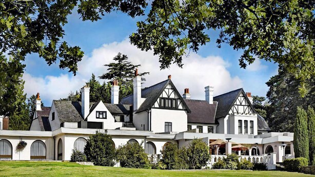 A large, multi-story house with a white facade, multiple chimneys, and a well-maintained lawn. - Hilton Cobham (Cobham)